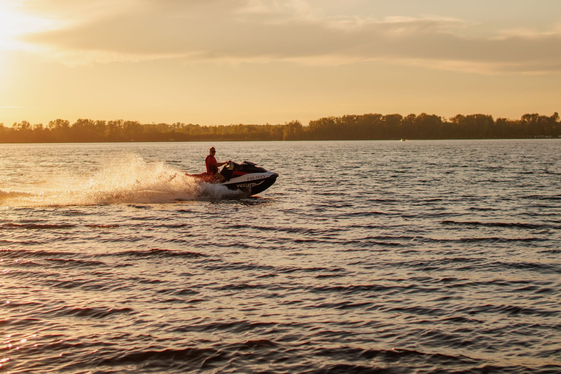 A jet ski speeds across a lake at sunset, with water splashing behind, jet ski dock perth