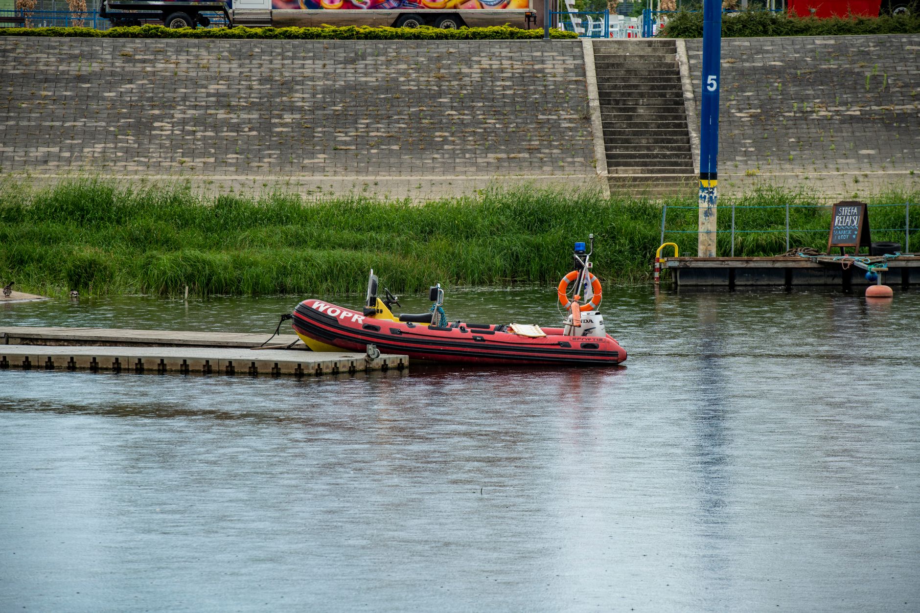 A rubber raft moored at a pontoon on a calm river with canal views and lush green riverbank, floating dock perth