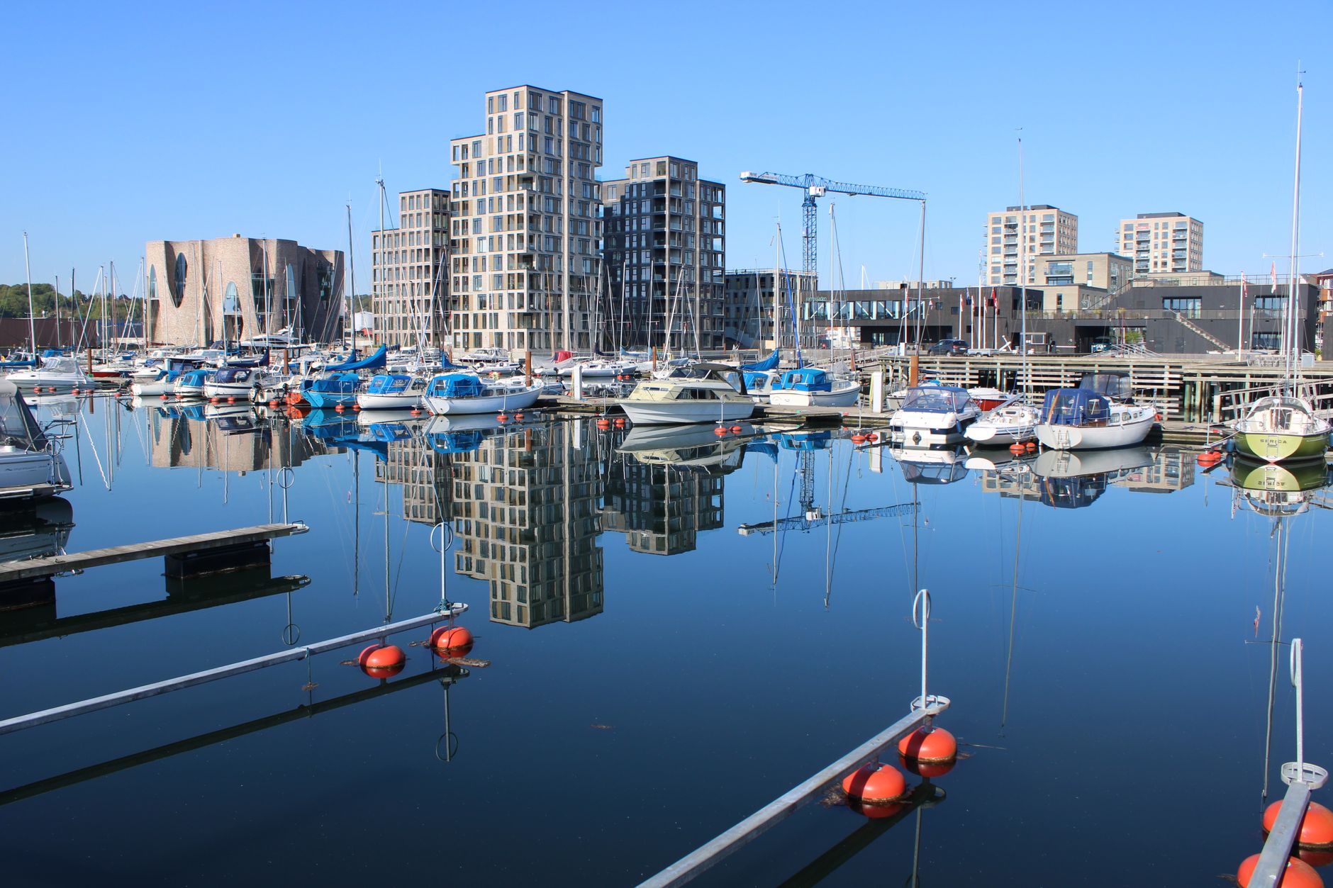 Boats moored in Vejle's harbor, reflecting modern buildings under a clear sky, how a sinking system docks a heavy boat