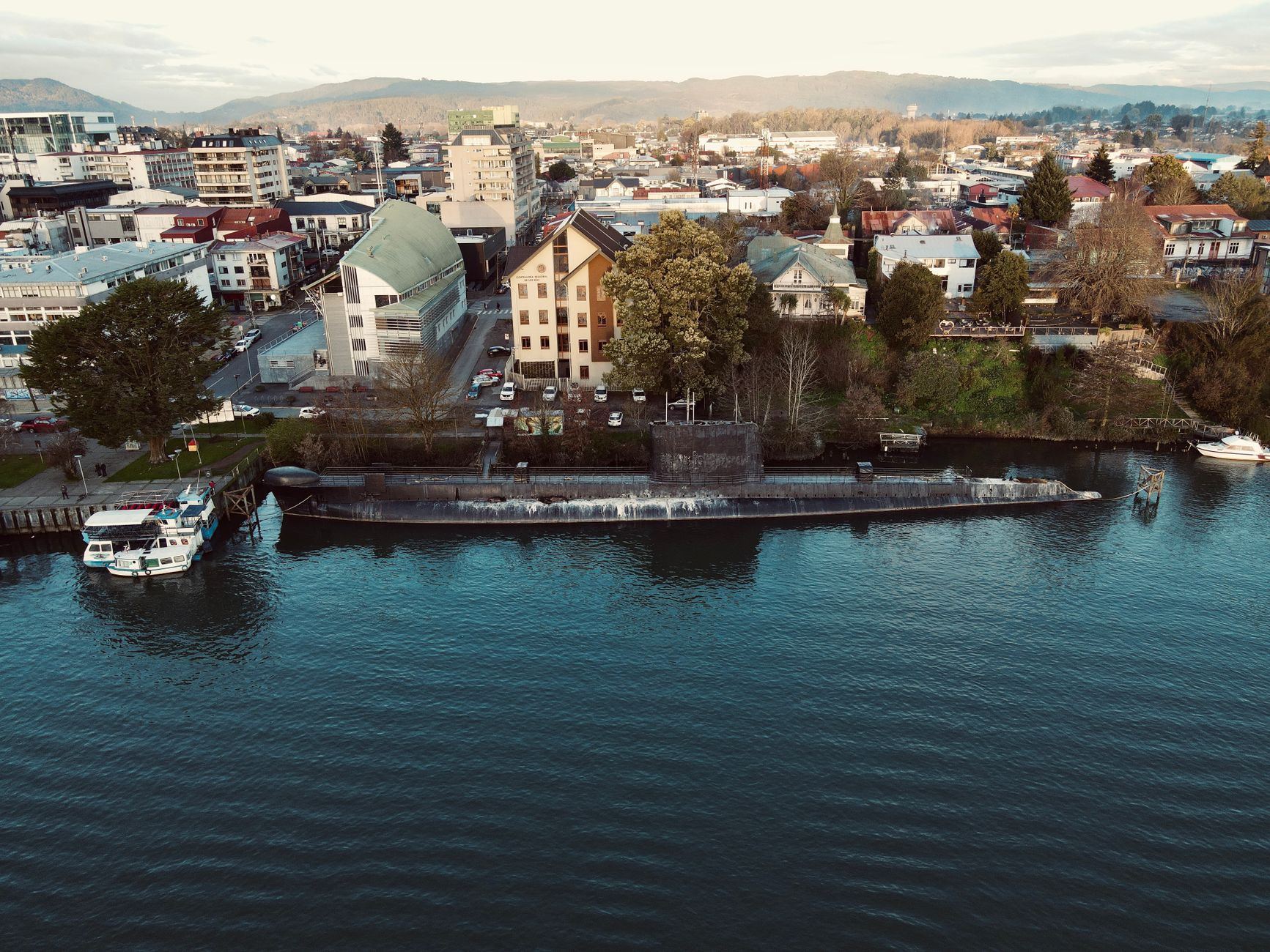 Aerial view of Valdivia, Chile, featuring a submarine docked along the waterfront amidst urban architecture.